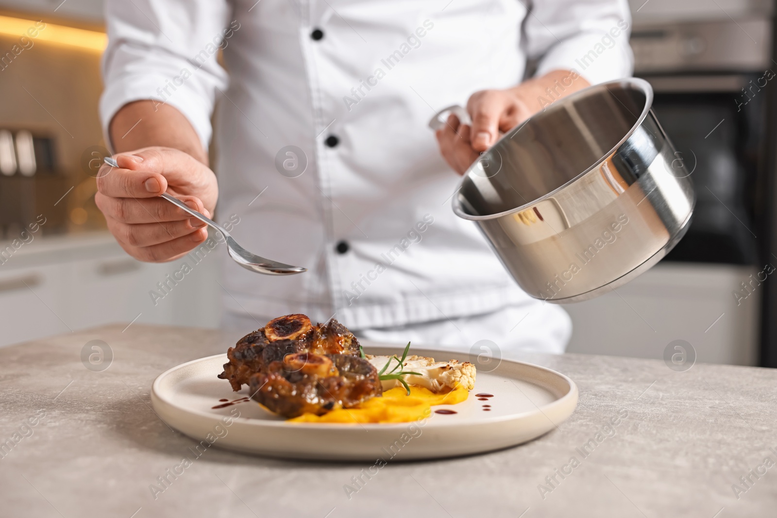 Photo of Professional chef adding sauce to delicious dish at table indoors, closeup