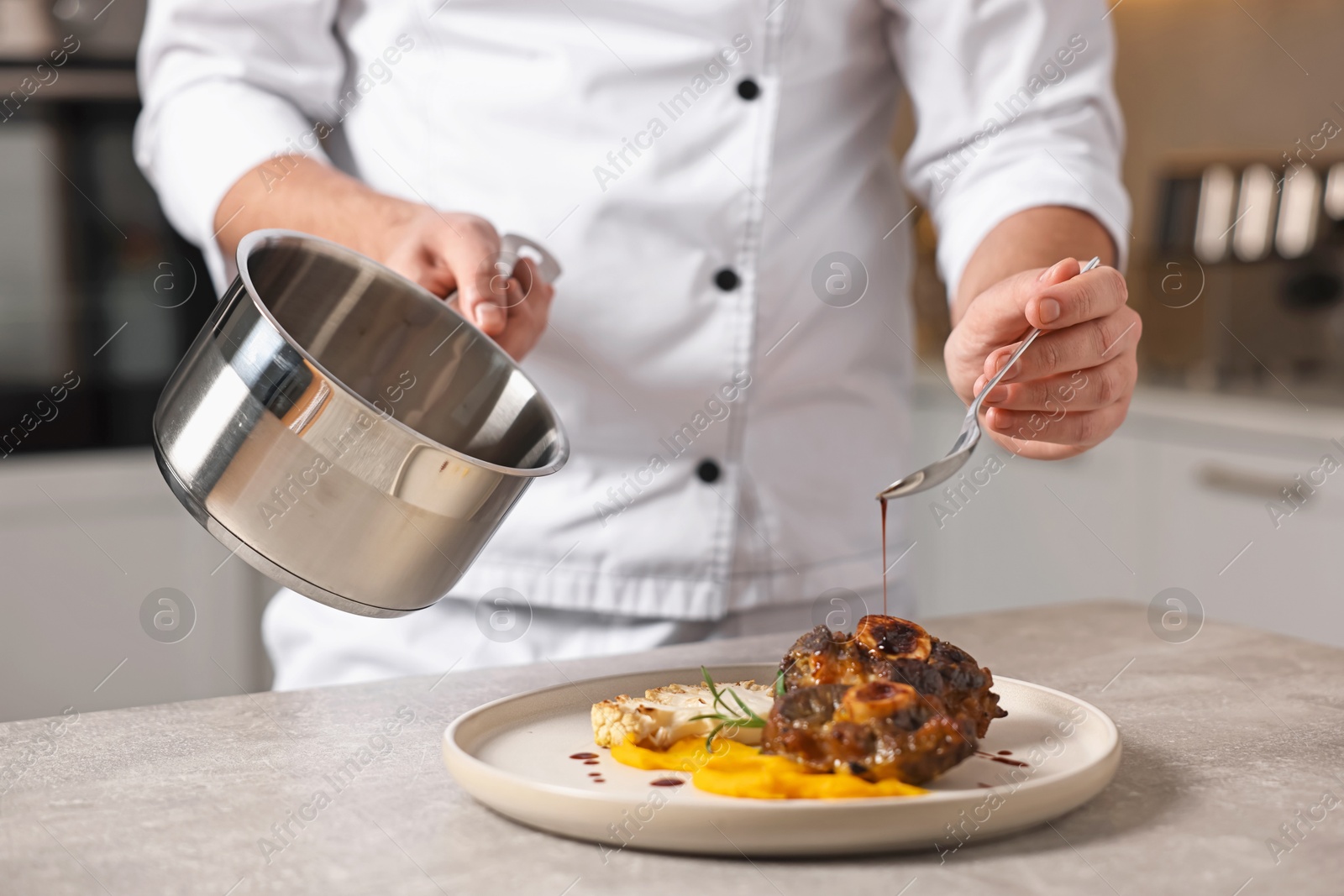 Photo of Professional chef adding sauce to delicious dish at table indoors, closeup