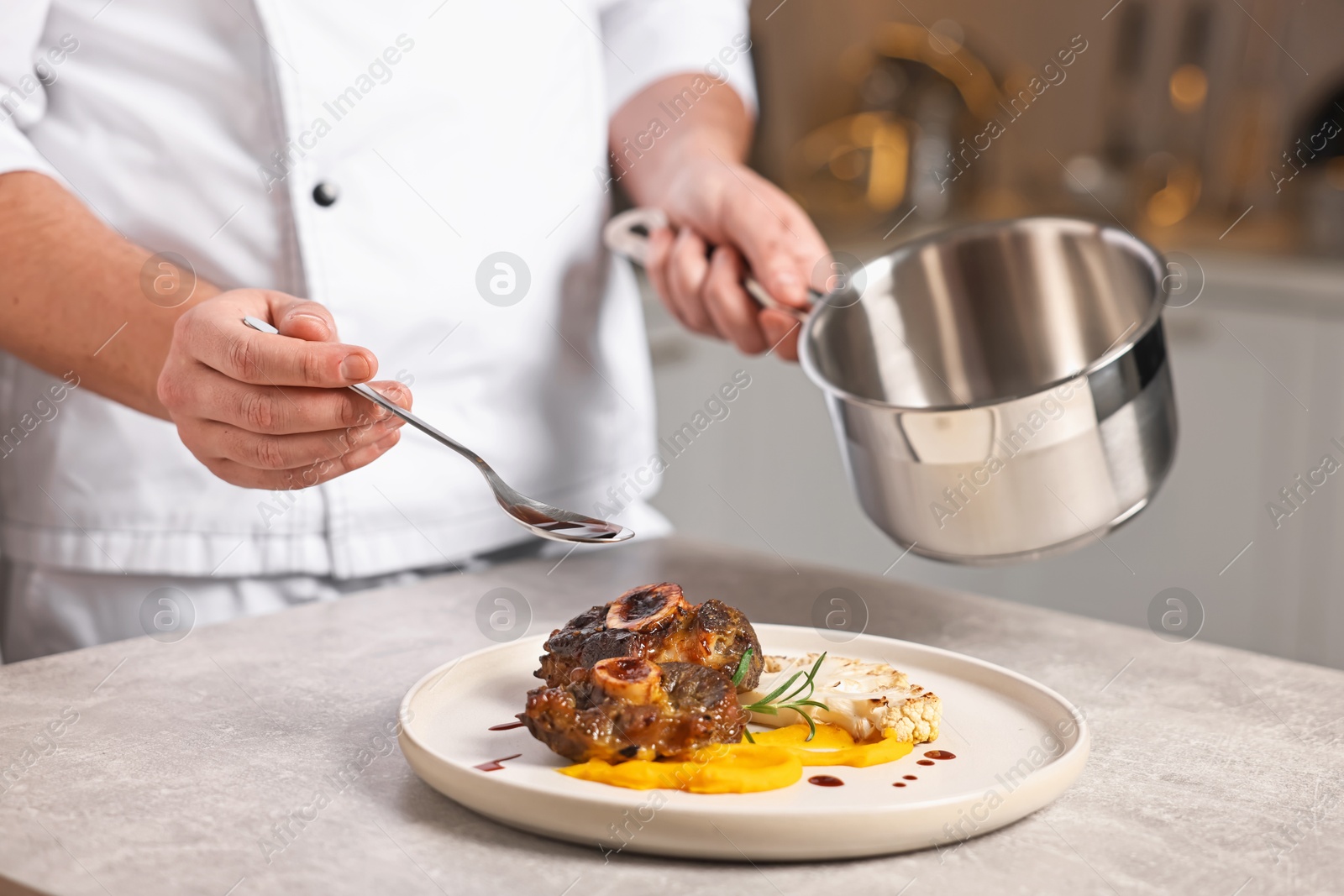 Photo of Professional chef adding sauce to delicious dish at table indoors, closeup