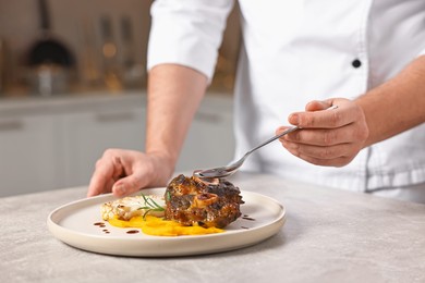 Photo of Professional chef adding sauce to delicious dish at table indoors, closeup