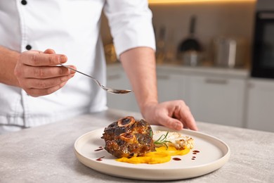 Photo of Professional chef adding sauce to delicious dish at table indoors, closeup