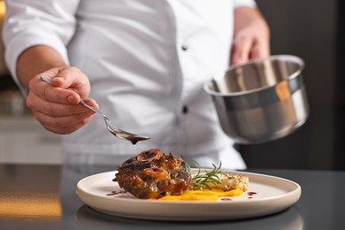 Photo of Professional chef adding sauce to delicious dish at table indoors, closeup