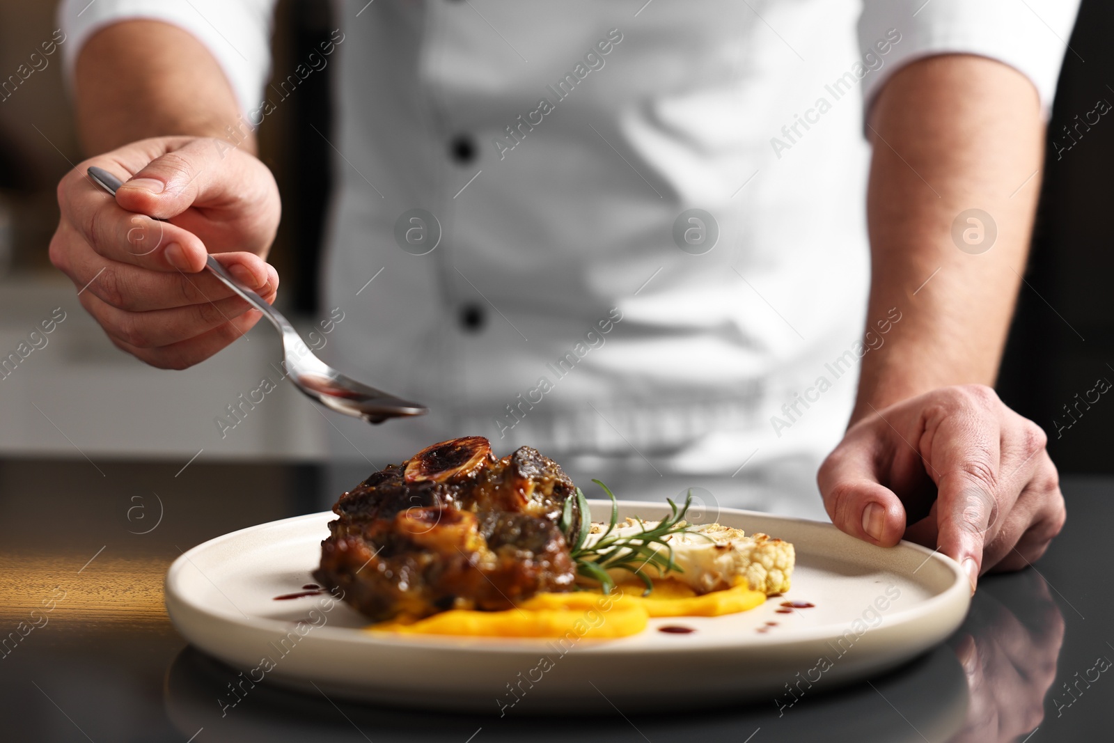 Photo of Professional chef adding sauce to delicious dish at table indoors, closeup