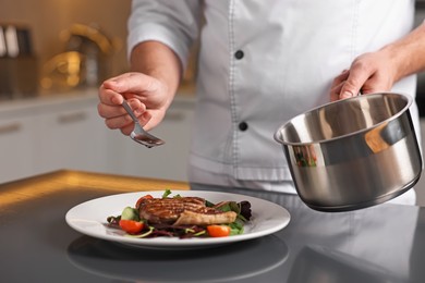 Photo of Professional chef adding sauce to delicious dish at table indoors, closeup