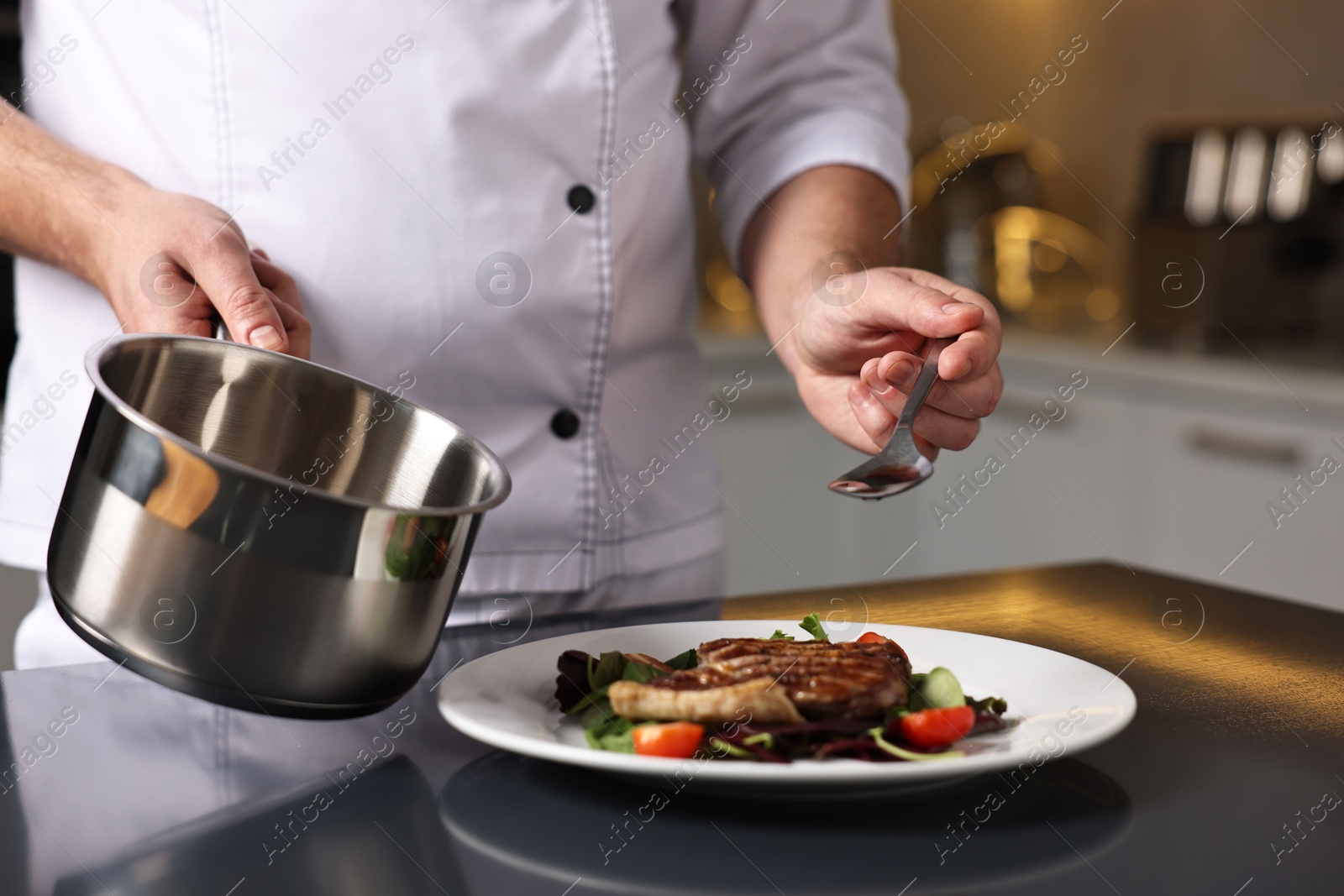 Photo of Professional chef adding sauce to delicious dish at table indoors, closeup