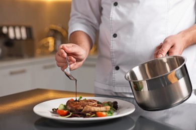 Photo of Professional chef adding sauce to delicious dish at table indoors, closeup