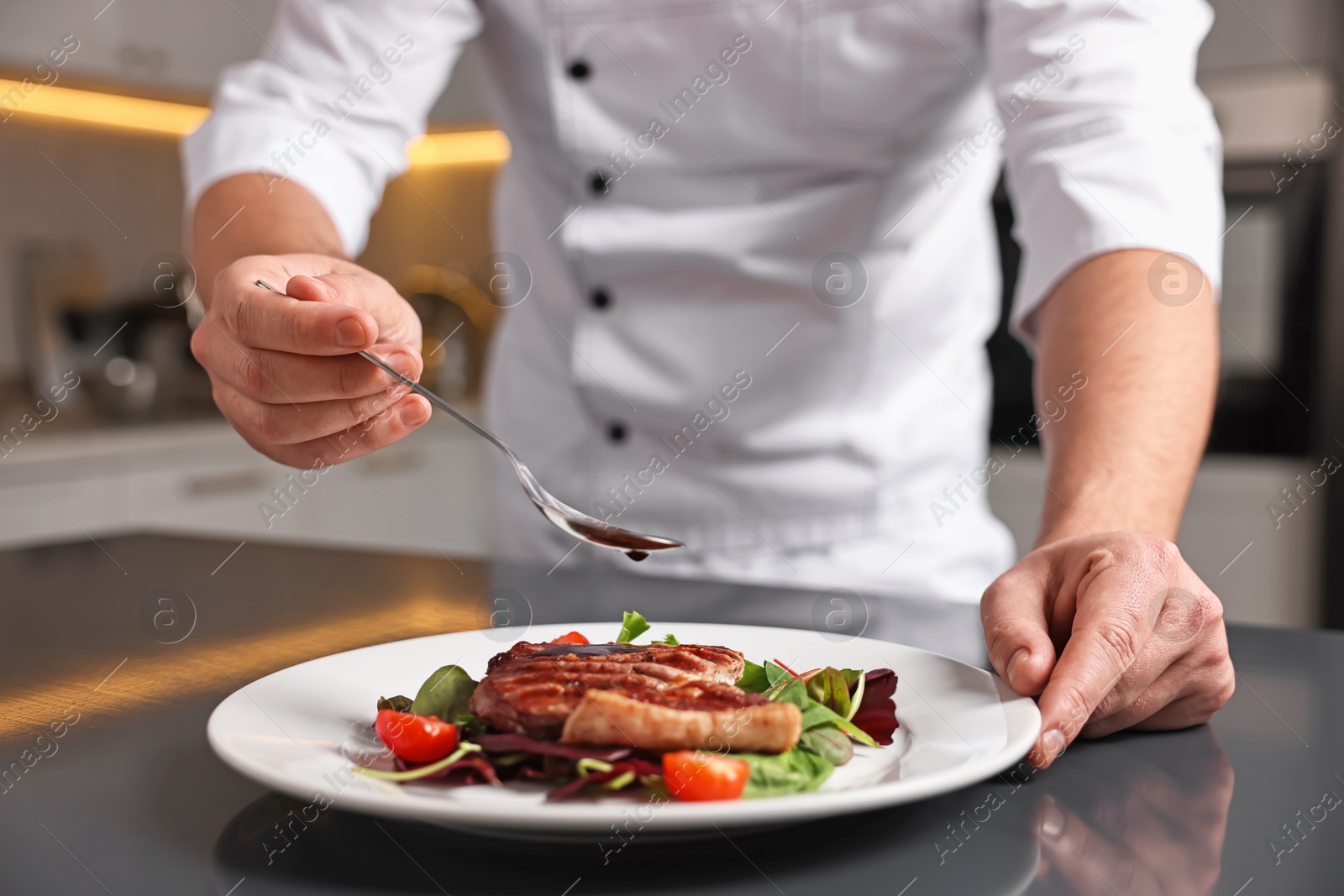 Photo of Professional chef adding sauce to delicious dish at table indoors, closeup