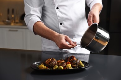 Photo of Professional chef adding sauce to delicious dish at table indoors, closeup