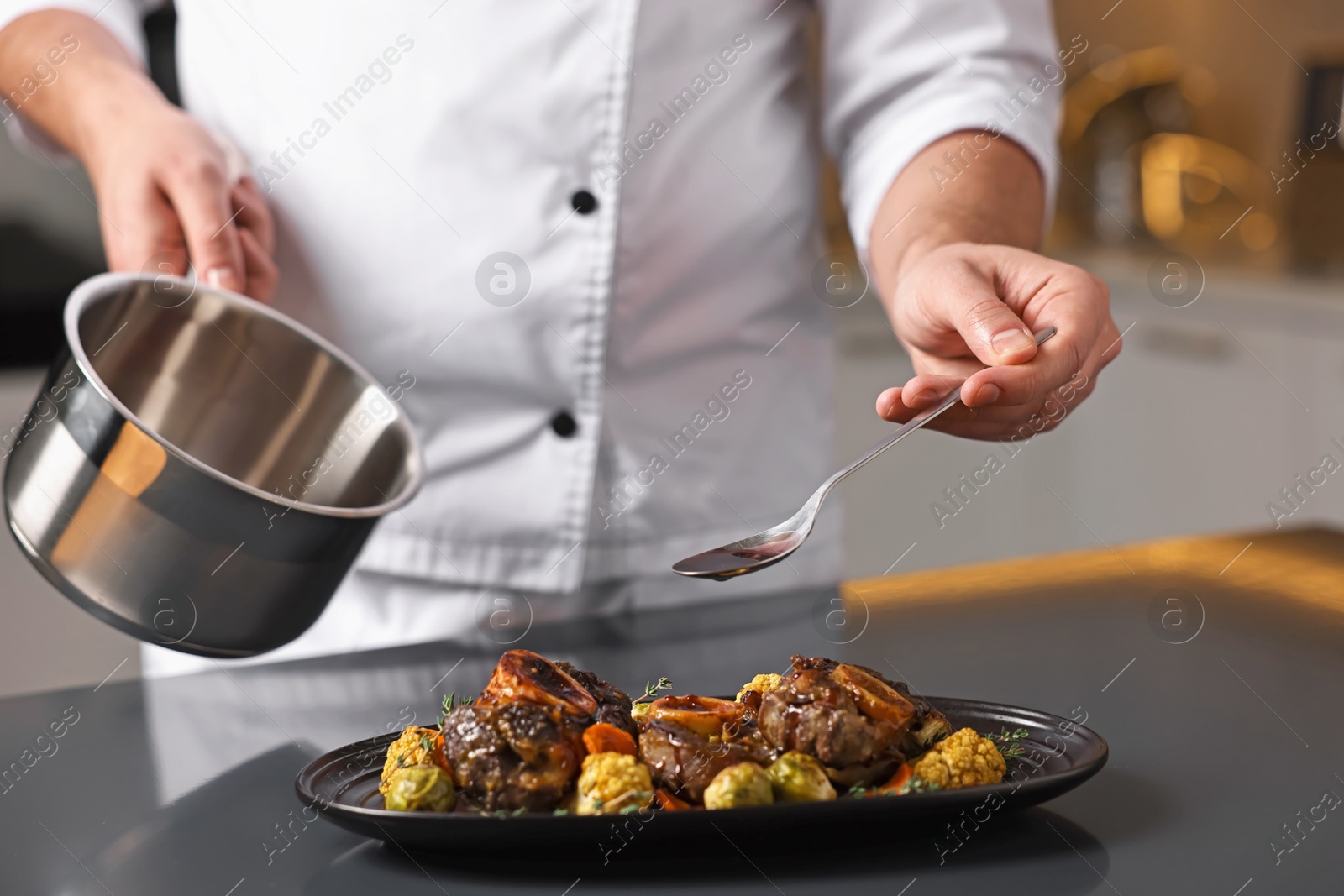 Photo of Professional chef adding sauce to delicious dish at table indoors, closeup