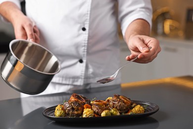 Photo of Professional chef adding sauce to delicious dish at table indoors, closeup