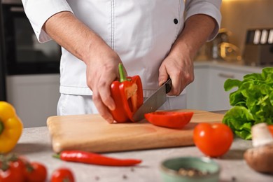 Photo of Professional chef cutting bell pepper at table in kitchen, closeup