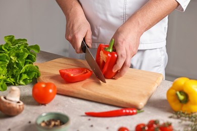 Photo of Professional chef cutting bell pepper at table in kitchen, closeup