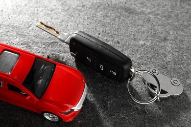 Photo of Car key and model on grey textured table, closeup. Buying auto