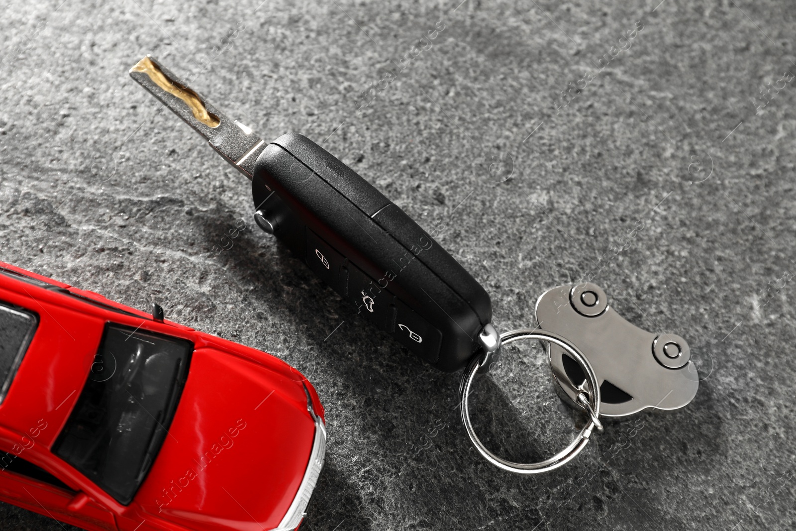 Photo of Car key and model on grey textured table, closeup. Buying auto