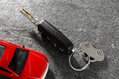 Photo of Car key and model on grey textured table, closeup. Buying auto