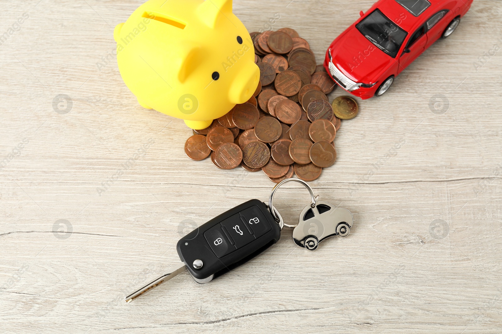 Photo of Car key, model, coins and piggybank on light wooden table, above view. Buying auto