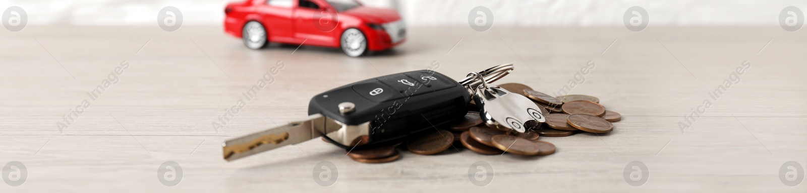 Photo of Car key, model and coins on light wooden table, selective focus. Buying auto