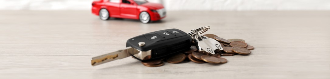 Photo of Car key, model and coins on light wooden table, selective focus. Buying auto