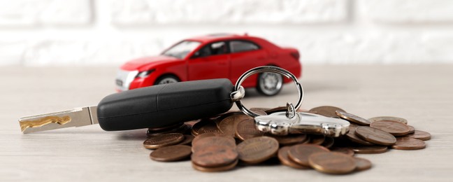 Photo of Car key, model and coins on light wooden table, selective focus. Buying auto