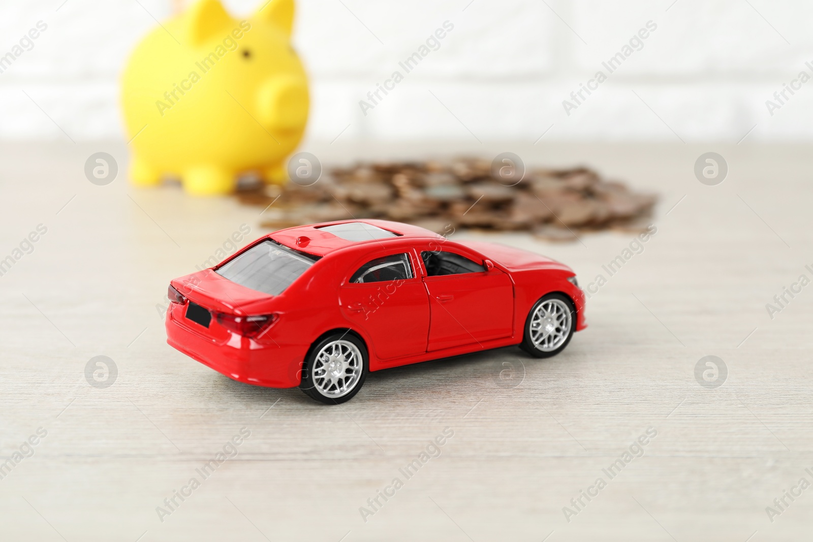 Photo of Car model, piggybank and coins on light background, selective focus