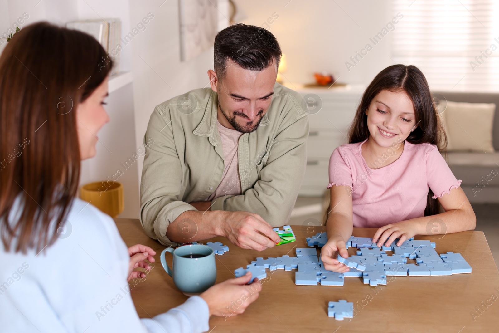 Photo of Happy parents and their daughter solving puzzle together at wooden table indoors