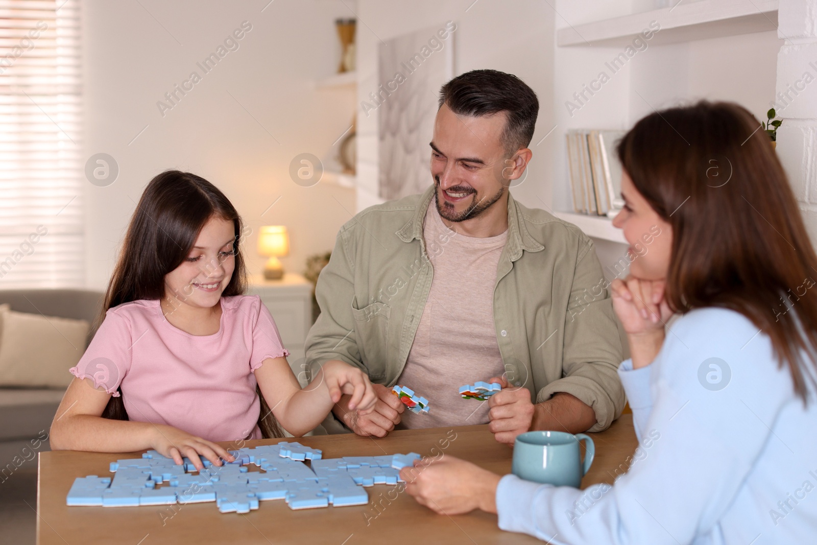 Photo of Happy parents and their daughter solving puzzle together at wooden table indoors