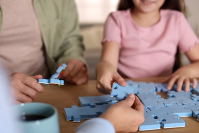 Photo of Parents and their daughter solving puzzle together at wooden table indoors, closeup