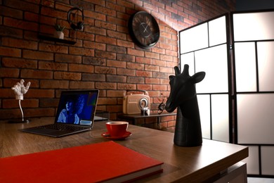 Photo of Book, laptop, cup of coffee and decor on wooden table near brick wall