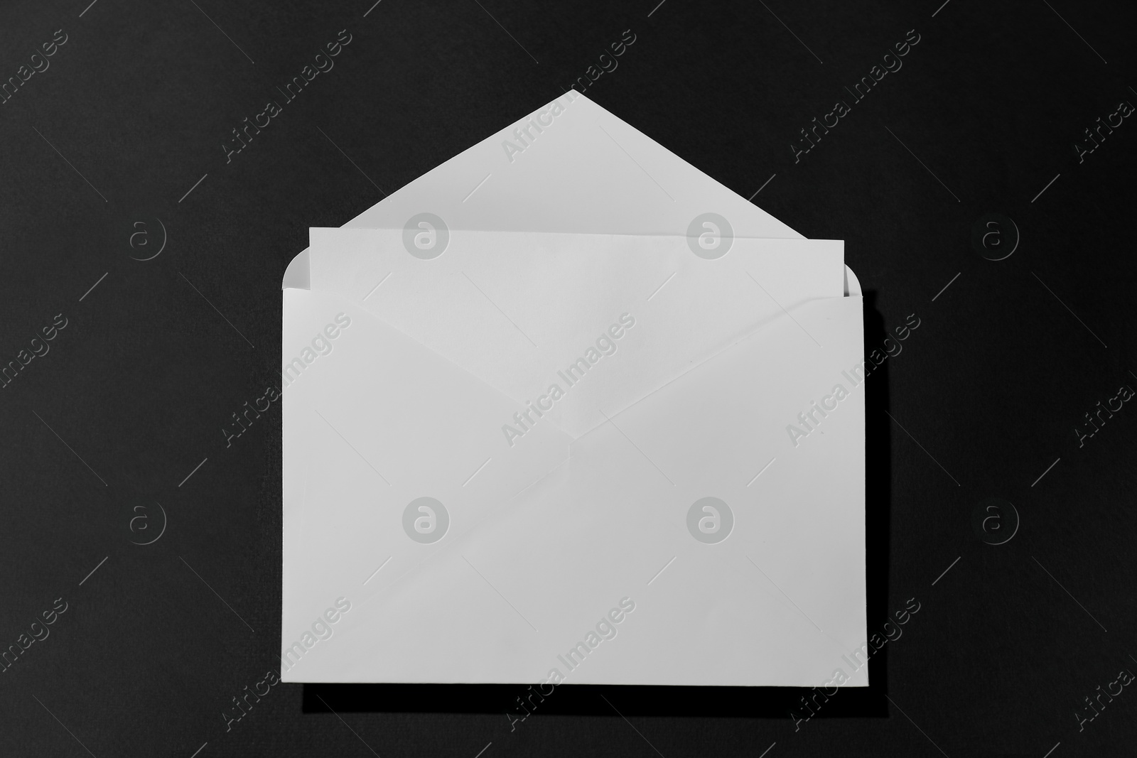 Photo of Paper envelope with letter on black background, above view. Mockup for design