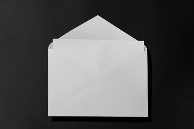 Photo of Paper envelope with letter on black background, above view. Mockup for design