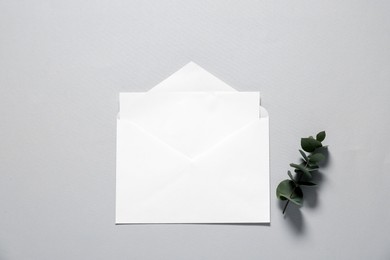 Paper envelope with letter and eucalyptus branch on gray background, flat lay. Mockup for design