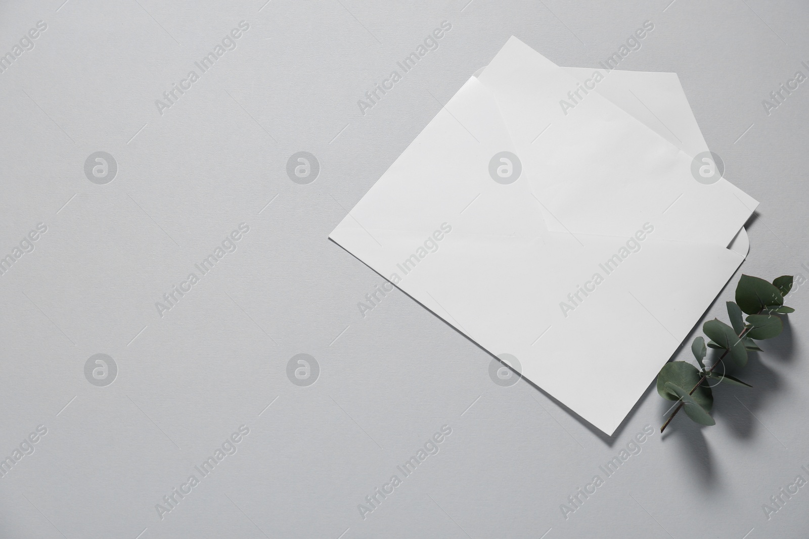 Photo of Paper envelope with letter and eucalyptus branch on gray background, flat lay. Mockup for design