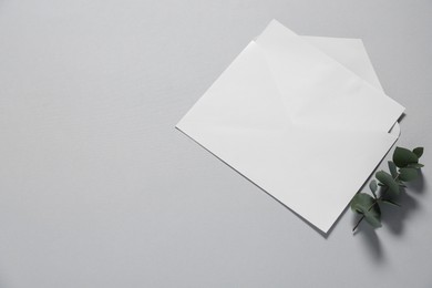 Paper envelope with letter and eucalyptus branch on gray background, flat lay. Mockup for design