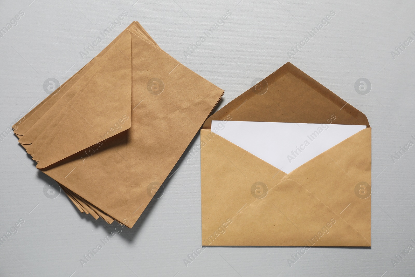 Photo of Kraft paper envelopes with letter on gray background, top view. Mockup for design