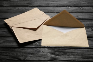 Photo of Kraft paper envelopes with letter on black wooden background. Mockup for design