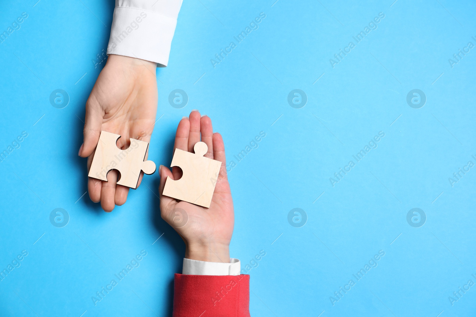 Photo of Business strategy and teamwork concept. Partners putting puzzle pieces together on light blue background, top view. Space for text