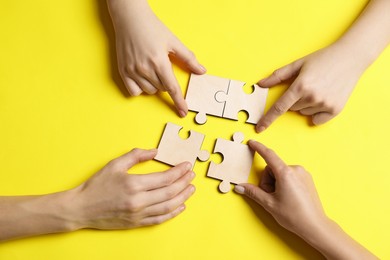 Photo of Business strategy and teamwork concept. Group of businesspeople putting puzzle pieces together on yellow background, top view