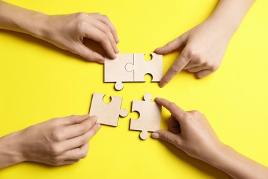 Photo of Business strategy and teamwork concept. Group of businesspeople putting puzzle pieces together on yellow background, top view