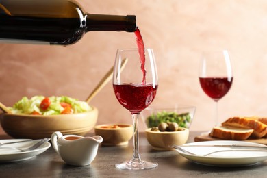 Photo of Pouring red wine into glass at grey table with tasty food, closeup