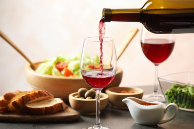 Photo of Pouring red wine into glass at grey table with tasty food, closeup