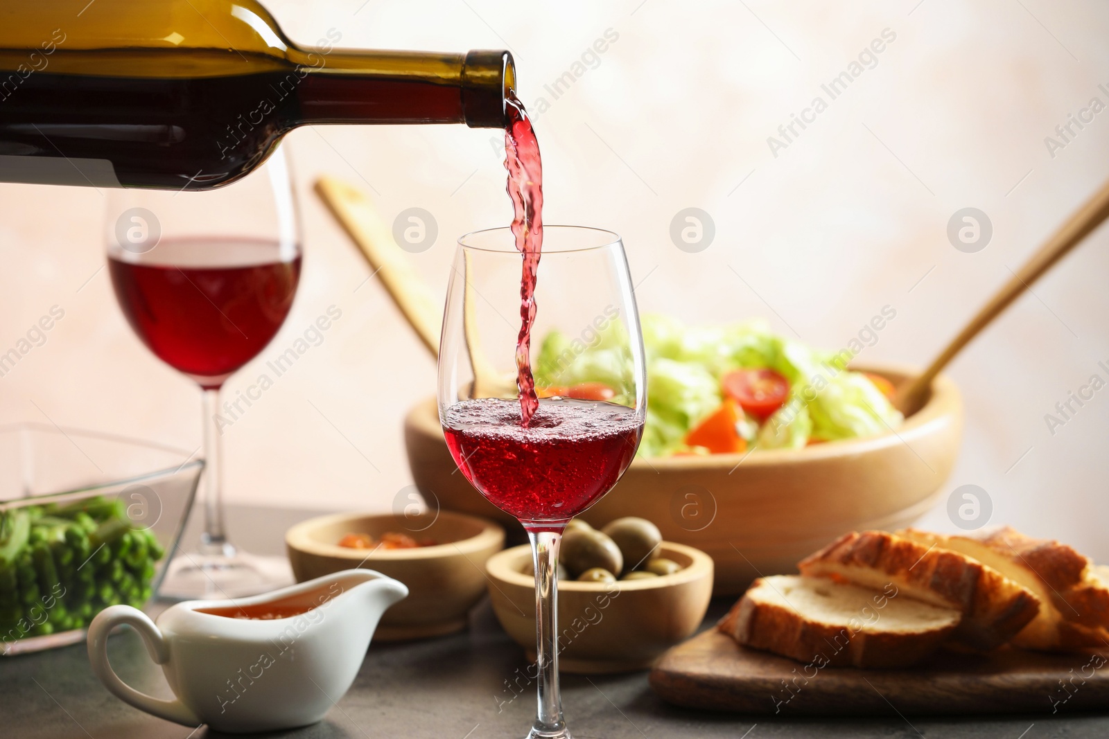 Photo of Pouring red wine into glass at grey table with tasty food, closeup