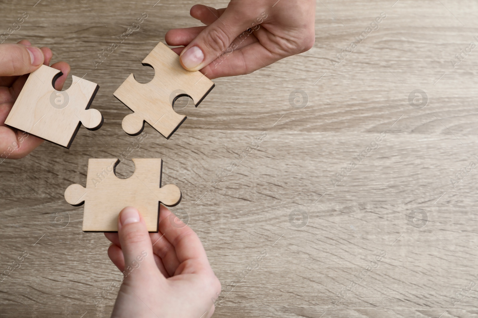 Photo of Teamwork. People putting puzzle pieces together at wooden table, top view. Space for text