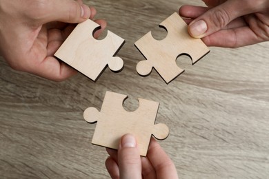 Photo of Teamwork. People putting puzzle pieces together at wooden table, top view