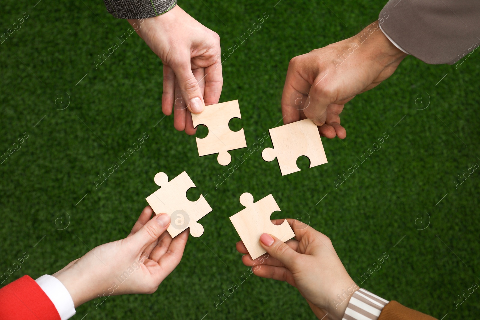 Photo of Teamwork. Group of people putting puzzle pieces together on blurred background, top view