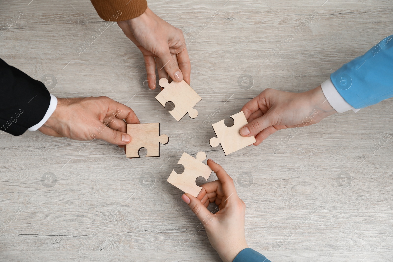 Photo of Teamwork. Group of people putting puzzle pieces together at wooden table, top view