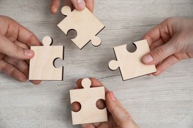 Photo of Teamwork. Group of people putting puzzle pieces together at wooden table, top view