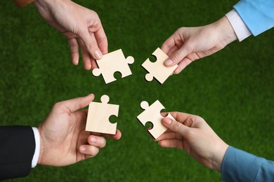 Photo of Teamwork. Group of people putting puzzle pieces together on blurred background, top view