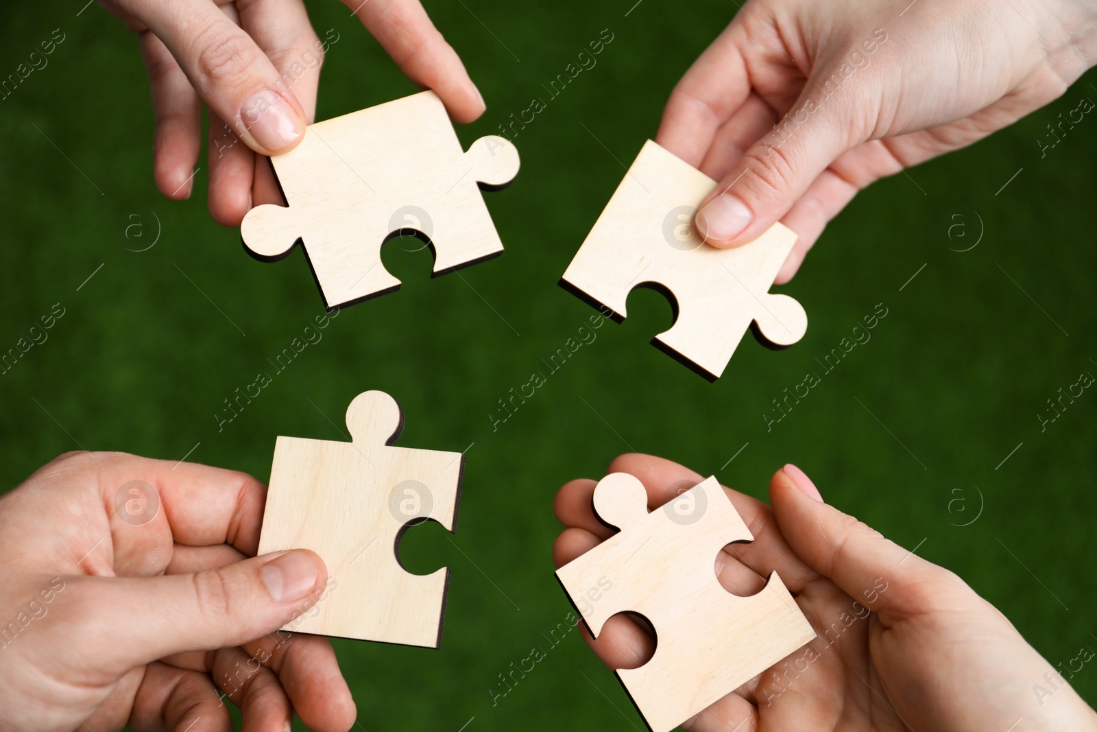 Photo of Teamwork. Group of people putting puzzle pieces together on blurred background, top view