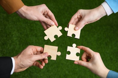 Photo of Teamwork. Group of people putting puzzle pieces together on blurred background, top view