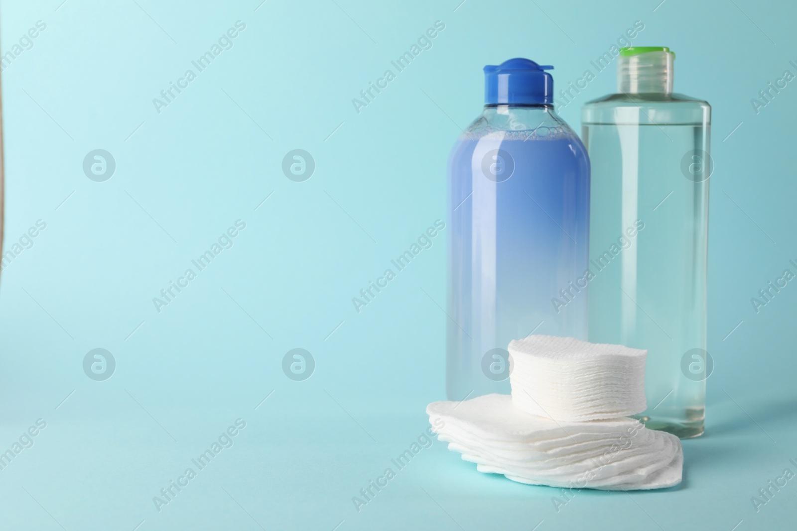 Photo of Clean cotton pads and micellar water on light blue background. Space for text